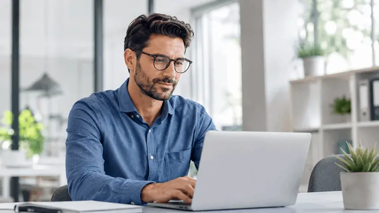 lentes_para_miopia_trabajo_computadora_ocumed_queretaro_550x310 Hombre con lentes trabajando frente a una computadora, imagen relacionada con el uso de lentes para Miopía y trabajo de cerca.
