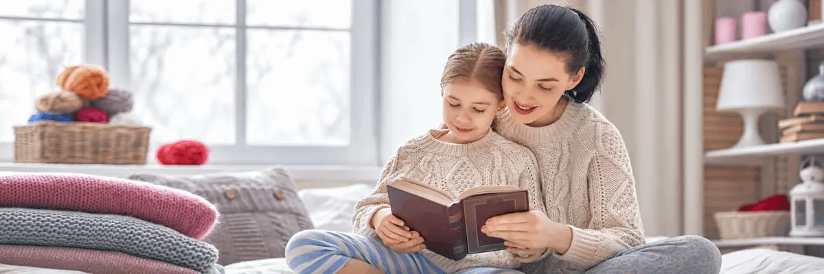 Madre e hija sonríen mientras leen juntas un libro en casa, imagen ilustrativa sobre la importancia de la visión cercana y la salud visual infantil.