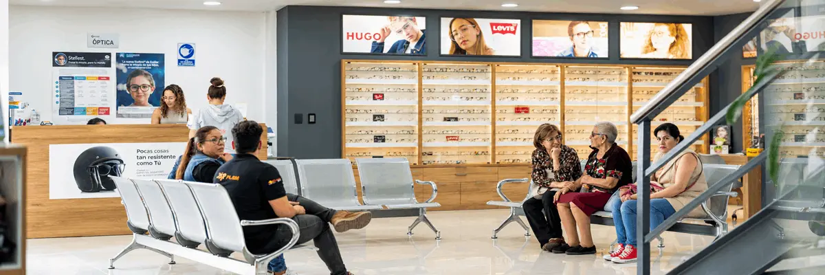 Sala de espera de una óptica moderna con pacientes sentados y exhibidores de lentes, imagen relacionada con la atención visual e hipermetropía en Querétaro.